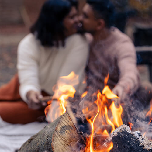 yaira_karin_nishi-107 Ein Mann und eine Frau schmoren Marshmallows ueber dem Feuer und kuessen sich dabei.